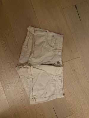 Beiga shorts från Pull&Bear - Säljer ett par beiga shorts från Pull&Bear i klassisk femficksmodell. De har råa kanter nertill och knapp- samt dragkedjestängning. Perfekta för varma dagar och har en enkel, stilren look.