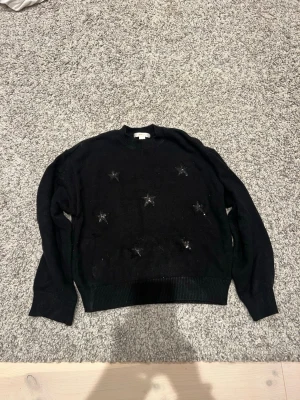 Svart stickad tröja med stjärnor - Snygg svart stickad tröja från Gina Tricot med glittriga stjärnor på framsidan. Tröjan har rund halsringning, ribbade muddar och är perfekt för dig som gillar en enkel men cool look. Passar till allt och är supermjuk.