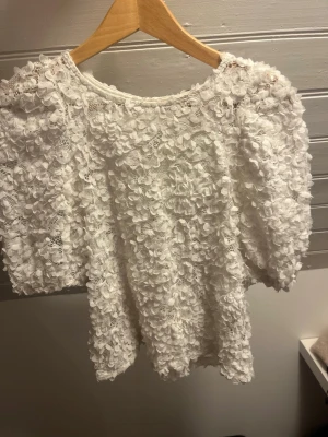 Vit blus med spets och volang - Supersöt vit blus med korta ärmar, täckt av blommig spets och volangdetaljer. 
