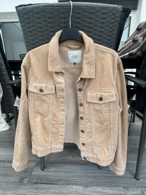 Beige jeansjacka från Jacqueline de Yong - Snygg beige jeansjacka i bredspårig manchester från Jacqueline de Yong. Klassisk modell med två bröstfickor med knappar, krage och knappstängning framtill. Perfekt för dig som vill ha en trendig och avslappnad look.