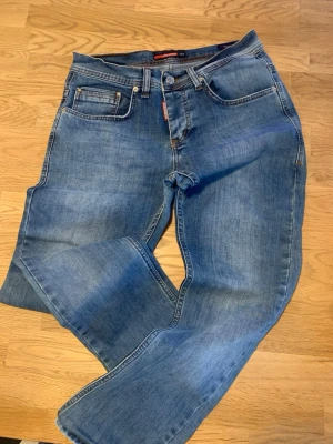 Blå raka jeans från DSQUARED2 Jeans - Säljer ett par klassiska blå jeans från Dsquared2 Jeans med rak passform och fem fickor. Jeansen har en snygg tvättad look, normal midja och detaljer i orange söm. Tillverkade i bomull för en skön känsla.