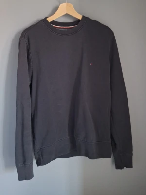 Mörkblå sweatshirt från Tommy Hilfiger - Klassisk mörkblå sweatshirt från Tommy Hilfiger med rund halsringning och diskret logga på bröstet. Tröjan har långa ärmar, ribbade muddar och är tillverkad i mjuk bomull. Perfekt för en avslappnad och stilren look.