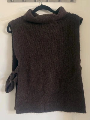 Brun stickad väst från Kappahl - Mysig brun stickad väst från Kappahl med hög krage och knytband i sidan. Perfekt att slänga över en skjorta eller tröja för en chill lager-på-lager-look. Ribbstickad struktur ger en snygg och enkel vibe.