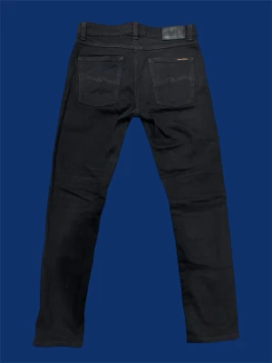  Nudie Jeans Lean Dean - Svarta jeans från Nudie Jeans i modellen 31/30. Jeansen har klassisk femficksdesign, svarta sömmar och Nudie Jeans logga på bakfickan. Tillverkade i ekologisk bomull med en straight passform som sitter snyggt. Perfekta för dig som gillar stilrena och enkla jeans.