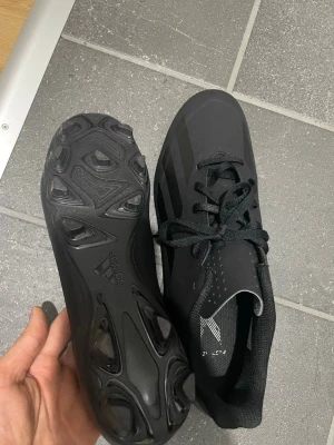 Svarta Adidas fotbollsskor - Säljer ett par helsvarta fotbollsskor från Adidas med klassiska tre ränder på sidan. Skorna har snörning, låg profil och dobbar i plast för bra grepp på planen. Materialet är syntetiskt och designen är stilren och sportig. 44 passar 45, helt nya köptes för 999