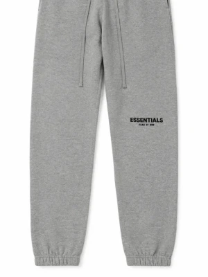 Grå Essentials mjukisbyxor - Snygga grå mjukisbyxor från Essentials Fear of God med tryckt logga på benet. Byxorna har dragsko i midjan och resår vid bensluten för en skön och avslappnad passform. Perfekta för chill dagar eller streetwear-stil.
