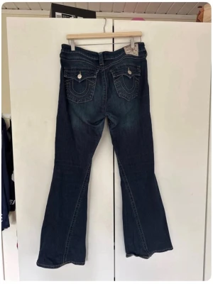 True Religion Joey Low Rise Flare Jeans - Säljer ett par mörkblå True Religion Joey jeans med låg midja och utsvängda ben. Dom är nästan helt nya men säljer då de är lite för stora för mig. 