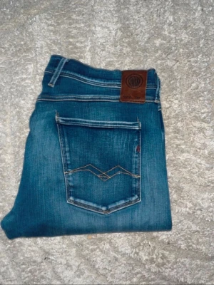 Replay Anbass jeans  - Midja 46cm! Snygga blå slim fit jeans från Replay med klassisk femficksdesign och dekorativa sömmar på bakfickan. Jeansen har en något tvättad look och är tillverkade i stretchigt denimtyg för extra komfort. (Se hål på ena knäet) JAG SKICKAR EJ FLER BILDER PÅ JEANSEN! för storleksguide hänvisar jag till måtten och för bättre inblick i passformen rekommenderar jag att googla på modellnamnet. :) 1,107