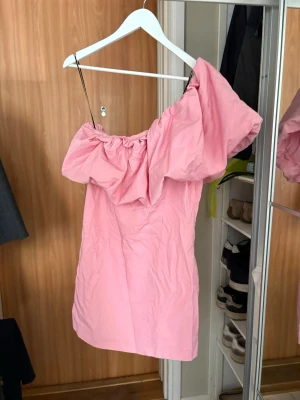 Rosa offshoulder kort klänning - Supersöt rosa kort klänning med offshoulder-design och voluminös volang upptill. Klänningen har en figurnära passform och är perfekt för dig som vill sticka ut. Endast använd en gång, lite skrynklig. från H&M 