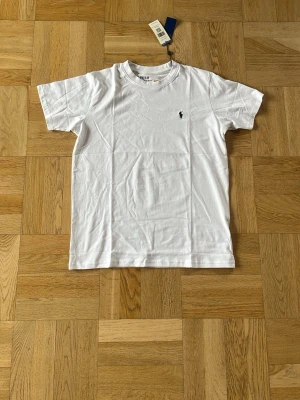 Vit t-shirt från Polo Ralph Lauren - Klassisk vit t-shirt från Polo Ralph Lauren med rund hals och den ikoniska broderade loggan på bröstet. Tillverkad i mjuk bomull och har en normal passform. Perfekt basplagg för alla tillfällen.