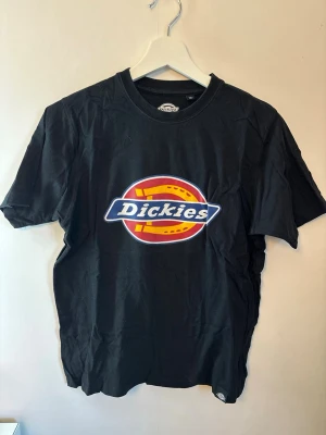 Svart Dickies t-shirt  - Klassisk svart t-shirt från Dickies med stor färgglad logga på bröstet. T-shirten har rund hals och korta ärmar, tillverkad i mjuk bomull för en skön och avslappnad stil.