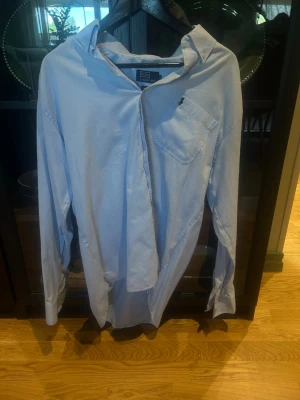 Ljusblå skjorta från Polo Ralph Lauren - Klassisk ljusblå skjorta från Polo Ralph Lauren i 100% bomull. Skjortan har lång ärm, bröstficka och knappstängning framtill. Perfekt för en clean och stilren look. PRUTA!
