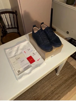 Christian Louboutin skor storlek 45 -  Säljer ett par Christian Louboutin, Snygga mörkblå sneakers i mocka med matchande mörkblå snören och röd sula, Storlek 45. Använda lite. Syns på sulan men fortfarande jättebra skick, vill bli av med dom så skicka bud, Kvitto, bag, låda samt kort finns och skickas med! 