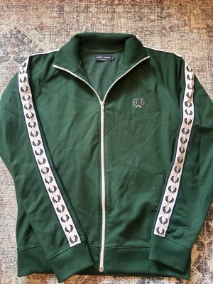 Fred Perry track jacket - Fred Perry Track Jacket – Mörkgrön – Stl L  Snygg och klassisk Fred Perry track jacket i mörkgrön färg 💚  • Storlek: L • Färg: Mörkgrön • Klassisk Fred Perry Laurel Wreath-design • Signatur-tape med loggan längs båda ärmarna • Hög krage • Full zip • Fickor på sidorna • Mycket snygg retro/sportswear-look  Mycket fint skick och redo för sin nya ägare. 📦 Snabb och smidig frakt 💬 Skicka gärna meddelande vid frågor!  #fredperry #fredperrytrackjacket #fredperryjacket #trackjacket #fredperryvintage 