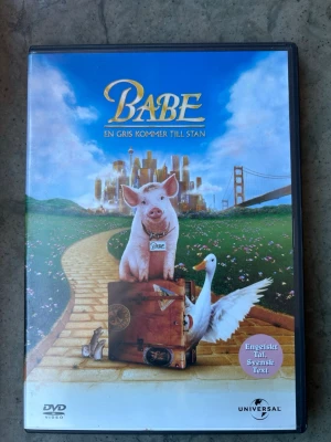 Babe: en gris kommer till stan DVD - DVD-film med "Babe: En gris kommer till stan". Filmen har engelskt tal och svensk text. Speltid: 1 timme 35 minuter. Åldersgräns: Från 6 år.  Finns på språk: Engelska, Tyska   OBS!! skivorna är begagnade så det kan förekomma repor/hairlines på skivorna, men då jag kollar igenom alla filmer jag säljer garanterar jag att alla funkar felfritt om inget annat står! :)