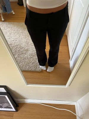 Svarta raka kostymbyxor - Säljer ett par svarta kostymbyxor med rak passform och klassisk midja. Byxorna har hällor för skärp och sidofickor. Perfekta för en clean och stilren look. Materialet är en mjuk och lite stretchig blandning.