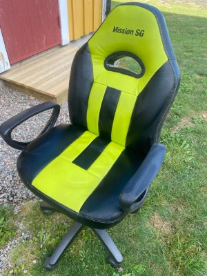 Gamingstol Mission SG - Säljer en gamingstol från Mission SG i svart och grön, konstläder med sportig design. Stolen har armstöd, hög rygg och hjul för enkel förflyttning. Perfekt för gaming eller som kontorsstol.