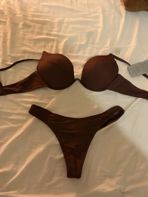 Brun push-up bikini med enkel design - Snygg brun bikini med push-up bygel-bh och matchande trosa. Enkel och stilren modell med smala axelband och utan extra detaljer. Perfekt för strandhäng eller pooldagar.
