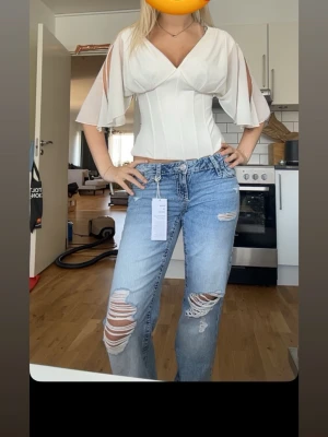 Blå slitna raka jeans med hål - Säljer ett par ljusblå jeans med raka ben och stora slitningar samt hål på båda benen. Jeansen har klassisk femficksmodell och normal midja. Perfekta för en avslappnad och trendig look.