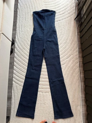Mörkblå denim jumpsuit Pull&Bear - Snygg mörkblå denim jumpsuit från Pull&Bear med utsvängda ben och hög midja. Gjord i stretchigt jeanstyg som sitter tajt upptill och har raka, långa ben. Perfekt för dig som gillar en trendig och bekväm look. Knappt använda💕helt i nyskick