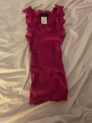 Rosa ribbad linnetopp från Rosemunde - Supersöt rosa linnetopp från Rosemunde med ribbad struktur och spetsdetaljer runt halsringningen och ärmhålen. Toppen är ärmlös och har en feminin, figurnära passform. Perfekt att styla med jeans eller kjol för en trendig look.