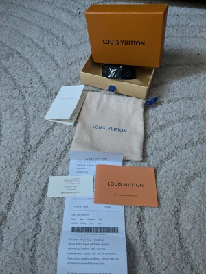  lv svart läderarmband - Snyggt svart armband i äkta läder med ikoniskt monogram och silverfärgad lv detalj framtill. Armbandet har klassisk design och levereras med original ask och dustbag. Perfekt accessoar för dig som gillar exklusiv stil.