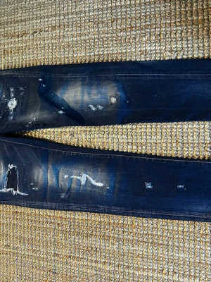 Mörkblå slitna jeans från Dsquared2 - Säljer ett par mörkblå jeans från Dsquared2 med slitningar och distressed detaljer längs benen. Jeansen har gul kontrastsöm, klassisk femficksmodell och knappgylf. Materialet är denim i bomull med en cool, trendig look.