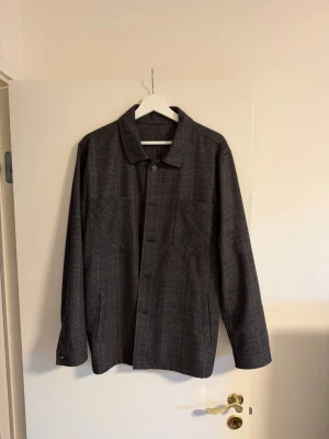 Overshirt Sand Copenhagen - Snygg mörkbrun overshirt med diskret rutigt mönster. Klassisk krage, knäppning framtill och två bröstfickor. Långärmad modell i ett mjukt material som känns lite tjockare, perfekt för lager på lager. Passar till många olika stilar.