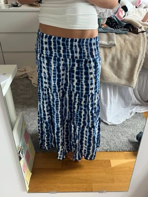 Blåvit långkjol med batikmönster - Säljer en flowy blåvit långkjol med batikinspirerat mönster. Kjolen har bred resår i midjan för skön passform och är tillverkad i ett mjukt, lätt material som passar perfekt till varma dagar. Perfekt att styla med en enkel topp eller crop top.
