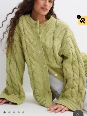 Grön kabelstickad kofta - Snygg kabelstickad kofta i ljusgrönt med stora träknappar framtill. Koftan har oversized passform, ribbade muddar och rund halsringning. Perfekt för lager på lager och ger en chill vibe till din outfit .slutsåld på hemsidan prislappen kvar. 