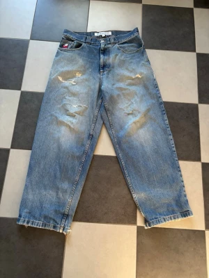 Blåa Bigboy jeans med slitningar - Säljer ett par blåa jeans från Bigboy i modell med raka ben och avslappnad passform. Jeansen har slitna detaljer och råa kanter vid bensluten för en trendig look. Klassisk femficksmodell i denim med knappgylf.