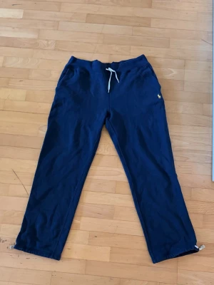 Mörkblå mjukisbyxor från Polo Ralph Lauren - Snygga mörkblå mjukisbyxor från Polo Ralph Lauren med gul broderad logga på vänster sida. Byxorna har dragsko i midjan och raka ben. Säljer för 600kr men priset kan diskuteras.