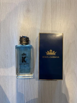 Dolce & Gabbana K Eau de Toilette 100ml parfym - Säljer en Dolce & Gabbana K Eau de Toilette 100ml parfym  med elegant blå flaska och en unik kronformad kork i guld och blå detaljer. Flaskan har en stilren design med svart logga och levereras i en lyxig mörkblå ask med gulddetaljer. Perfekt för dig som gillar exklusiva dofter.