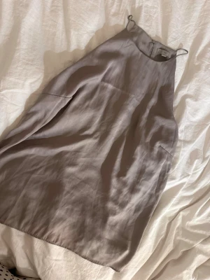 Beige ärmlös linnetopp - Säljer en stilren beige linnetopp med hög hals och smala axelband. Toppen är ärmlös och har en lös passform som ger en avslappnad vibe. Materialet känns svalt och mjukt, perfekt för varma dagar.