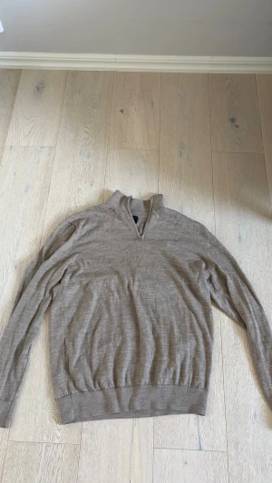 Beige stickad tröja med dragkedja H&M - Snygg beige stickad tröja från H&M med halv dragkedja vid halsen. Regular fit och långa ärmar. Perfekt till lager på lager och enkel att matcha med olika outfits. Tillverkad i mjukt material för skön känsla.