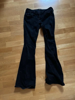 Svarta utsvängda jeans från true religion  - Säljer ett par svarta jeans med utsvängda ben från true religion. Jeansen har klassisk femficksdesign, hällor för skärp och stängs med knapp och dragkedja. Perfekta för dig som gillar en retroinspirerad look med mycket attityd.