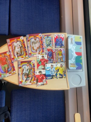 Panini FIFA samlarkort med box - Säljer ett gäng Panini FIFA samlarkort med färgglada motiv av olika fotbollsspelare. Kort i olika storlekar och design, vissa med LIMITED EDITION-tryck. Medföljer en snygg box med FIFA-logga och grafiskt mönster. Perfekt för dig som gillar att samla på fotbollskort. Allt för 400kr alltså alla kort på bilden. Styck kan man ge bud på 