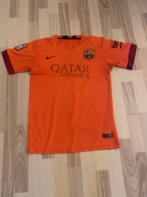 Barcelona Messi matchtröja orange - Snygg orange FC Barcelona matchtröja från Nike med Messi och nummer 10 på ryggen. Tröjan har Qatar Airways-tryck på framsidan, klubbmärke på bröstet och mörkröda detaljer vid ärmsluten. Perfekt för fotbollsträning eller att bära till vardags. Priset kan diskuteras😁