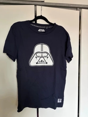 Mörkblå Star Wars t-shirt  - Cool svart t-shirt från Star Wars med en stor vit Darth Vader-ikon på bröstet. Klassisk passform. 