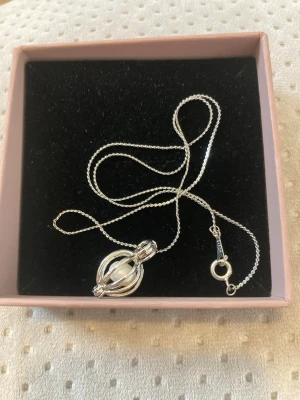 Halsband med pärlhänge - Snyggt halsband i vitguldplaterad 8 K med en kedja och ett hänge som omsluter en vit pärla. Hänget har en modern, rundad design och halsbandet har ett klassiskt lås. Perfekt accessoar för dig som gillar stilrena smycken med en twist.