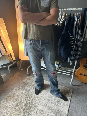 Nudie Average Joe - Nudie Jeans Average Joe – W33/L36  Average Joe i tvätten Org. Contrast Indigo, 100% ekologisk bomull.  Fint inslitna med mjuka kontrastfades och två synliga lagningar över knäna som ger paret ett unikt uttryck. Lagningarna är gjorda för att bäras, inte döljas.  Rak klassisk passform. Heelbite och naturlig patina genom hela jeansen.  Skick enligt bilder. Modellen på bilden är 183 cm.