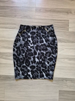 Kort leopardmönstrad kjol - Säljer en tight kortkjol med leopardmönster i svart och grå toner. Kjolen har en kroppsnära passform och är perfekt för dig som vill sticka ut med ett djuriskt print. Materialet känns mjukt och stretchigt, vilket gör den bekväm att bära.