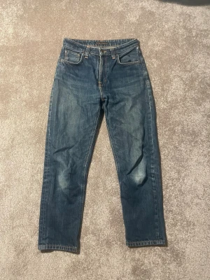 Blå raka jeans med kontrastsömmar - Säljer ett par klassiska blå jeans med raka ben och snygga kontrastsömmar. Jeansen har fem fickor, normal midja och slitningar på framsidan för en cool look. Materialet är kraftig denim i bomull. Perfekta till vardagsstilen!