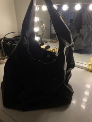 Svart slouchy handväska i skinnimitation - Säljer en svart slouchy handväska i mjuk skinnimitation med bred axelrem och magnetknäppning. Väskan har ett rymligt huvudfack och innerficka med dragkedja. Perfekt för dig som gillar en avslappnad men ändå stilren look.