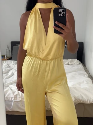 halterneck jumpsuit - Snygg gul jumpsuit med halterneck och djup v-ringning. Säljer pga den ej kommer till användning och den har bara använts 1 gång!