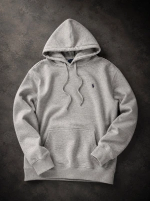 Grå hoodie med broderad logga - Säljer en stilren grå hoodie med huva och dragsnören. Tröjan har en broderad logga på bröstet och en stor magficka framtill. Tillverkad i mjukt sweatshirtmaterial och har ribbade muddar vid ärmar och nederkant. Perfekt för en avslappnad look. Lite knopprig längs ner