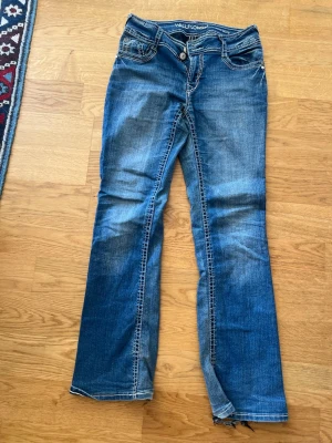 Blå bootcut jeans från Wallflower - Snygga blå bootcut jeans från Wallflower med slitningar och kontrastsömmar. Jeansen har broderade bakfickor med dekorativa detaljer och klassisk femficksdesign. Perfekta för en avslappnad och trendig look. Storlek 9 eftersom de är köpta i USA med passar som 38
