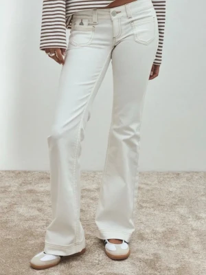 Vita bootcut jeans med låg midja - Säljer ett par vita bootcut jeans med låg midja och klassiska fem fickor. Jeansen har ljusa sömmar och är tillverkade i ett mjukt denimtyg med lite stretch för skön passform. Perfekta för en clean och trendig look.