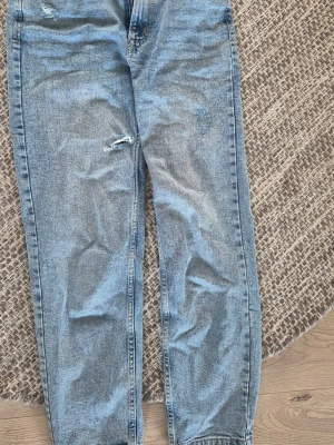 Ljusblå raka jeans från Pull&Bear - Säljer ett par ljusblå raka jeans från Pull&Bear med slitningar på låret och klassisk femficksmodell. Jeansen har hög midja och är tillverkade i denim med en avslappnad passform. Perfekta för en casual look.