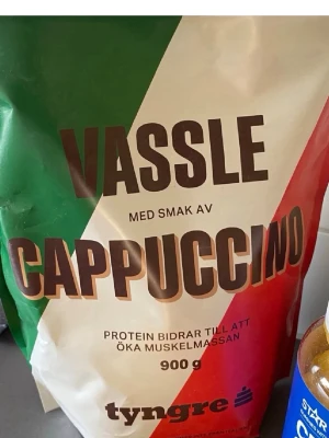 Vassleprotein cappuccino 900g - Oöppnad Vassleproteinpulver från Tyngre med cappuccinosmak. Förpackningen är 900 gram och har färgerna grön, vit och röd. Perfekt för dig som vill boosta din träning med extra protein och gillar kaffesmak.